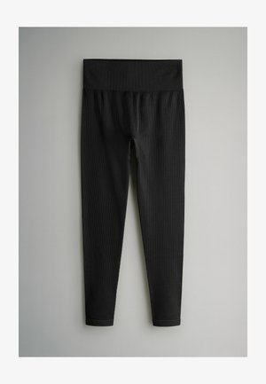 Melnas legingas ar platu elastīgo jostasvietu, izgatavotas no teksturēta auduma un cieši pieguļošas. Nav redzamu rakstu vai metāla detaļu.