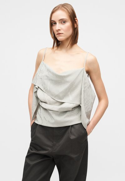 Blusa cinza clara sem mangas com um design em camadas com padrões subtis de texto, complementada por alças finas tipo spaghetti.