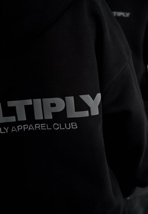 Felpa nera con testo grigio "MULTIPLY" e "APPAREL CLUB" ricamato sotto. Texture morbida, vestibilità casual, design minimalista.