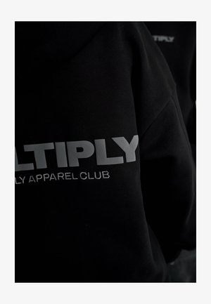 Felpa nera con testo grigio "MULTIPLY" e "APPAREL CLUB" ricamato sotto. Texture morbida, vestibilità casual, design minimalista.
