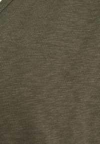 Nærbillede af olivengrønt strikket stof, der viser detaljeret tekstur og søm mønster.