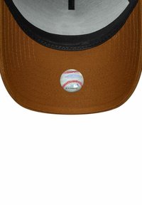Bruine baseballpet met een zwart vizier, voorzien van een ronde patch met een honkbalontwerp aan de voorkant. Tekst en afbeelding zijn zichtbaar op de patch.