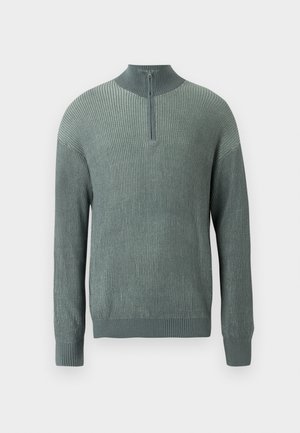 Žalias raukšlėtas megztinis su aukštu apykakle ir pusiau užtrauktuku priekyje. Su ilgomis rankovėmis ir tekstūrine mezgimo raštu.