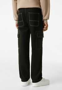 Black cargo pants with white stitching, featuring multiple pockets and a loose fit. Paired with white sneakers for contrast.
