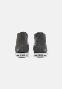 Visoke sive platnene tenisice s bijelim gumeni potplat, s Converse All Star brendingom. Strana nudi okrugli logotip.