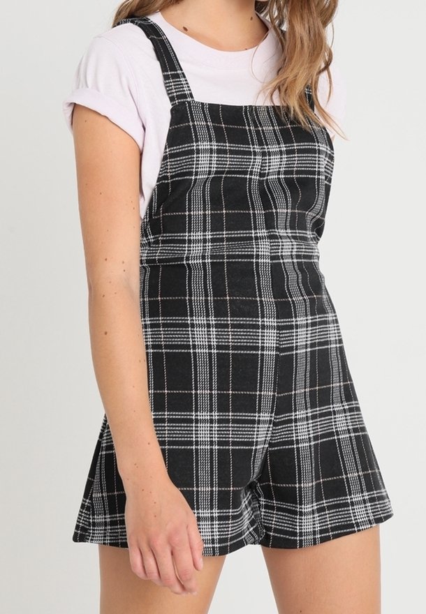 Schwarz-weiße karierte Latzshorts mit einem figurbetonten Schnitt und verstellbaren Trägern. Hergestellt aus einem weichen Stoff mit einer glatten Textur.