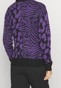 Lila und schwarze gemusterte Strickjacke mit einem wellenförmigen Tierdruckdesign, gerippten Cuffs und einem enganliegenden schwarzen Bund, aus gestricktem Stoff gefertigt.