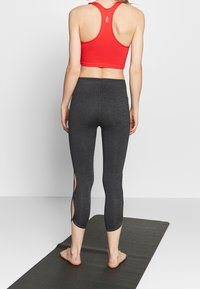 Röd räfflad sportcroptop och svarta capribyxor med sidoslitser, placerade på en yogamatta, som framhäver det stretchy tyget och den färgade designen.