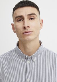 Chemise à col en bleu clair et rayures blanches. Présente un design à boutons, un col standard et une texture de tissu lisse.