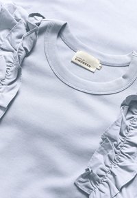 Ljust blå ribbad topp med volangärmar. Etiketten visar "KAREN BY SIMONSEN," storlek M. Slät textur med subtil lyster.