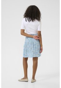 Floral skirt with a blue, white, and green pattern, knee-length, made of lightweight fabric, paired with a fitted white top and beige flat shoes.
