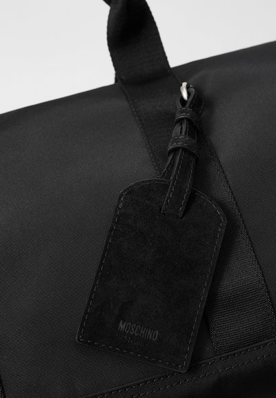 Black nylon bag with a textured surface, featuring a suede luggage tag embossed with "Moschino." Adjustable fabric handles for versatility.
