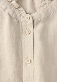 Ljusbeige linneskjorta med en volangkrage och fyra knappstängningar fram. Subtil textur med en något genomskinlig look.