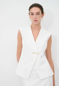Top bianco senza maniche con scollatura a V, dotato di una chiusura con accento dorato e forma strutturata. Tessuto liscio e opaco.