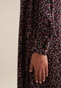 Abito a maniche lunghe con un motivo a pois multicolore su sfondo scuro. Presenta un polsino con bottoni e una texture di tessuto liscia.