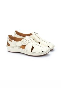 White leather shoes with open design, circular buckle detail, and decorative stitching along the sole. Brown interior lining.
