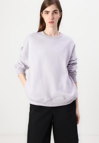 Ljuslila sweatshirt med långa ärmar, rund halsringning och ribbade muddar. Kombinerad med svarta vida byxor. Mjukt, texturerat tyg.