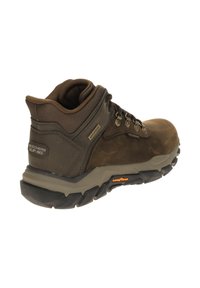 Brown waterproof hiking boot with a high collar, textured leather and mesh upper, metal eyelets, and a thick rubber traction outsole.