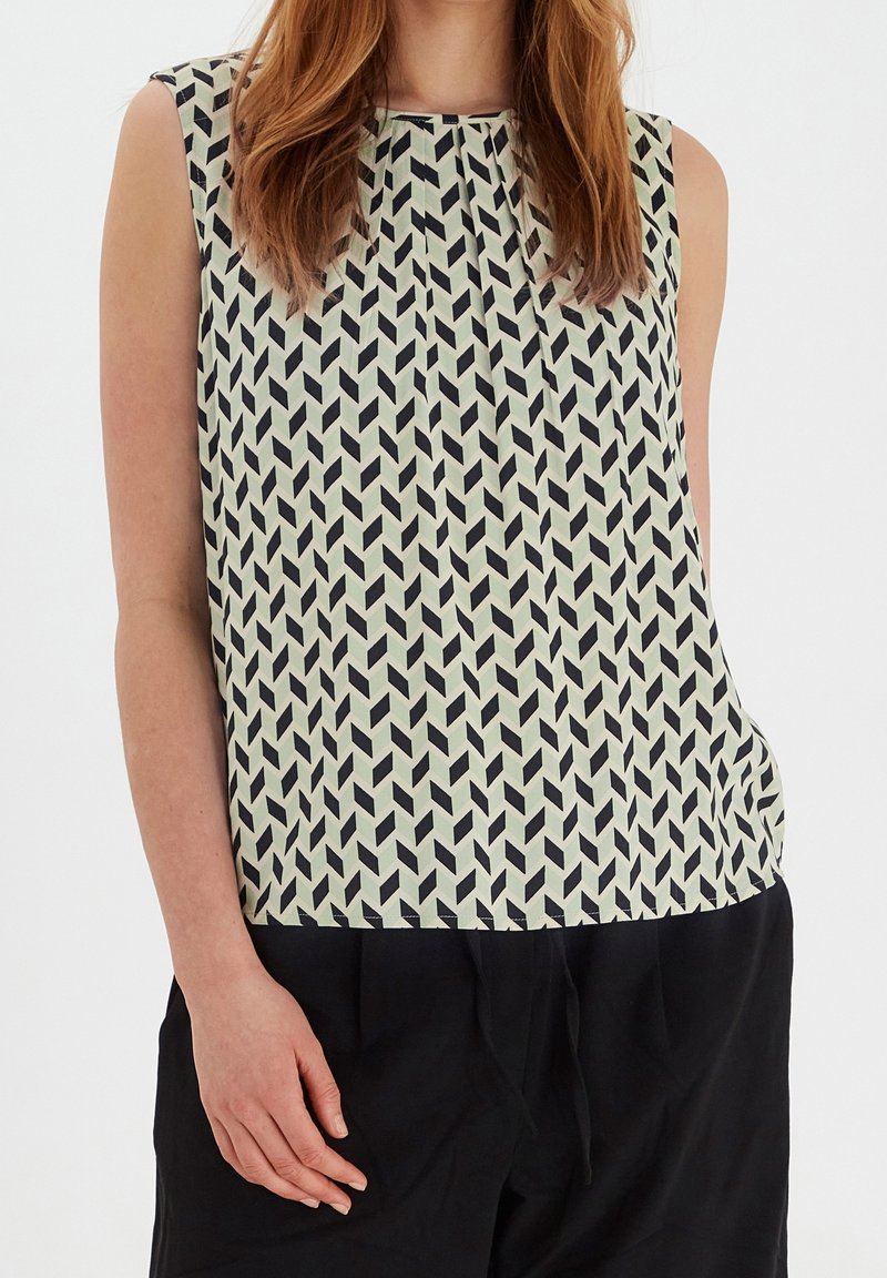 Haut sans manches crème avec motif chevron géométrique noir, porté avec un pantalon noir.