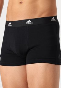 Juodos medvilnės bokso apatiniai šortai su juodu elastingu juosmeniu, ant kurio yra Adidas logo. Lygi tekstūra ir tvirtas prigludimas. Siuvimo linijos matomos virš šlaunies.