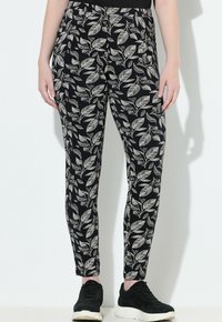 Zwarte broek met een wit bladerenpatroon, tapering fit, elastische tailleband en zachte stof, gecombineerd met zwarte sneakers.