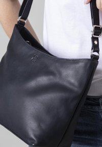 Black leather shoulder bag with a smooth texture, featuring a silver-tone adjustable strap and embossed logo on the front.