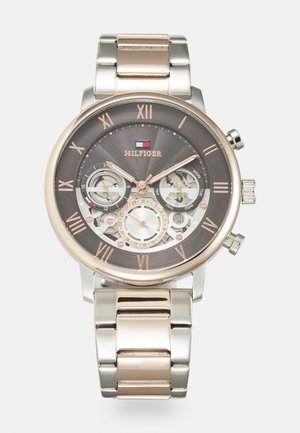 Montre chronographe avec un bracelet en acier inoxydable et or rose, cadran gris, design squelette, chiffres romains et trois sous-cadrans.