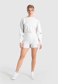 Witte lange mouw top met elastische taille, gecombineerd met bijpassende witte shorts. Beide hebben eenvoudige, strakke lijnen en minimalistische ontwerpelementen.