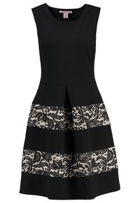 Ärmlös svart klänning med utställd kjol som har växlende enhetliga och blommönstrade spetsmönstrade horisontella paneler.