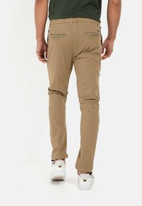 Khakihosen mit Slim Fit, elastischem Bund und zwei Gesäßtaschen. Kombiniert mit weißen Sneakers mit schwarzen und goldenen Akzenten.