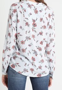 Blouse à manches longues à motif floral et rayé, avec des fleurs rouges et bleues, tissu doux, poignets à boutons et ourlet incurvé.