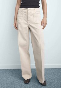Beige wide-leg jeans made of cotton twill. Features two front pockets and a button closure. Smooth texture with a straight, tailored fit.