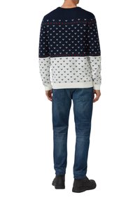 Sweter dzianinowy w poziome paski w kolorach granatowym, białym i czerwonym, z geometrycznym wzorem. Ściągacz przy kołnierzu i mankietach; zestawiony z niebieskimi dżinsami.