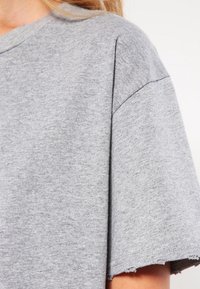 Graues Baumwoll-T-Shirt mit lockerer Passform, kurzen Ärmeln, sichtbaren Nähten und einem rohen Saum. Weicher Stoff und lässiges Design.