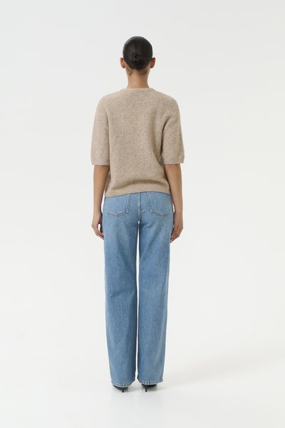Pull en tricot beige à manches bouffantes courtes et jeans larges bleu clair avec poches arrière, présenté de dos sur un fond neutre.