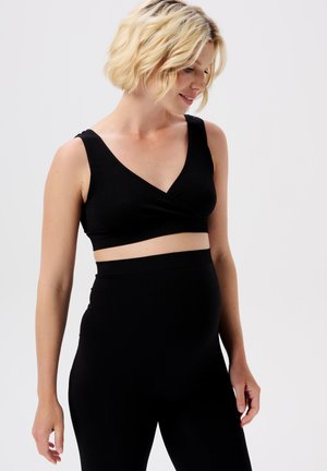 Schwarzes geripptes Crop-Top mit V-Ausschnitt und breiten Trägern, kombiniert mit hochgeschnittenen, passenden Leggings. Weicher Stoff, keine sichtbaren Muster oder Beschläge.