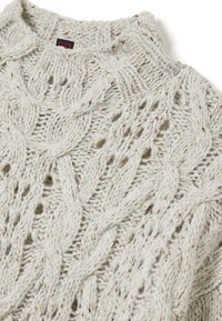 Pull en maille torsadée crème avec un motif texturé et des éclats dorés. Doté d'une encolure haute et d'une coupe ample et confortable.