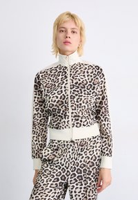 Leopard print zip-up jacket with high collar, fitted cuffs, and matching pants. Made of smooth fabric with a soft texture. Accented with cream details.