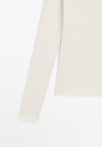 Bluzka z długim rękawem w jasnobeżowej mieszance bawełny, charakteryzująca się gładką teksturą i dopasowanym krojem, z prostym dołem i brakiem widocznych zdobień.