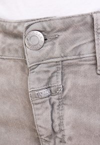 Šedé bavlněné kalhoty s kovovým knoflíkovým zapínáním, boční kapsou a prošitými detaily. Na štítku je nápis "CLOSED." Měkký, strukturovaný povrch.