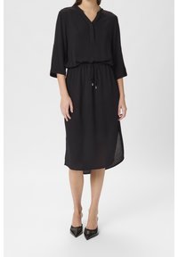 Abito nero realizzato in un tessuto leggero, con scollatura a V, maniche a tre quarti, vita con cordoncino e spacchi laterali, abbinato a tacchi a punta.