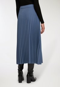 Gonna midi plissettata in morbido tessuto blu, con vita alta e design fluido. Abbinata a stivali neri al ginocchio con tacco.