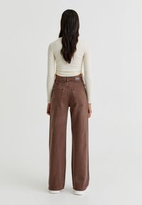 Ruskeit levelegge bukser med høy midje, fire lommer og subtile sømdetaljer, kombinert med en tettsittende lysfarget topp.