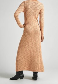 Lång, stickad orange klänning med vertikal ribbning, långa ärmar och ett spetsliknande mönster på ryggen; parat med svarta ankelskor.