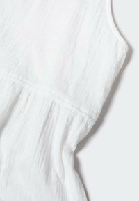 Top bianco senza maniche realizzato in un tessuto leggero e testurizzato, con dettagli arricciati in vita e un aspetto morbido e stropicciato.