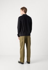 Fekete, hosszú ujjú ing gallérral, olívazöld nadrággal párosítva. Az outfitt slim fit és minimalista dizájnnal rendelkezik.