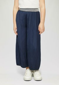Marineblauwe plooibroek met een metalen tailleband, met een losse pasvorm, textuurstof en een gezoomde broekspijp. Gepaard met witte sneakers.