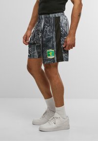 Mørkeblå og grå mønstrede shorts med elastisk talje, mesh-sider og et grønt logo-patch. Båret med hvide sneakers og ankelsokker.