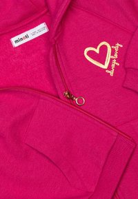 Felpa con zip fucsia caratterizzata da una grafica a forma di cuore dorato e dal testo "sempre adorabile", con etichetta tessuta che indica il marchio "minoti".