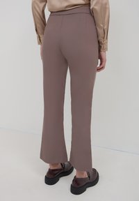 Pantalons marron ajustés à taille haute avec un design élégant, des bas évasés et une texture lisse. Associés à des chaussures sombres et robustes.
